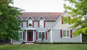 Front view of home with large lawn, burgundy window shutters, and gray house siding